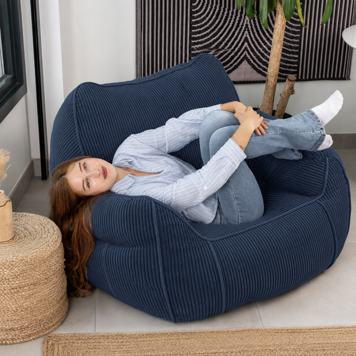 Personne assise sur le pouf fauteuil en velours côtelé bleu foncé, dans un salon