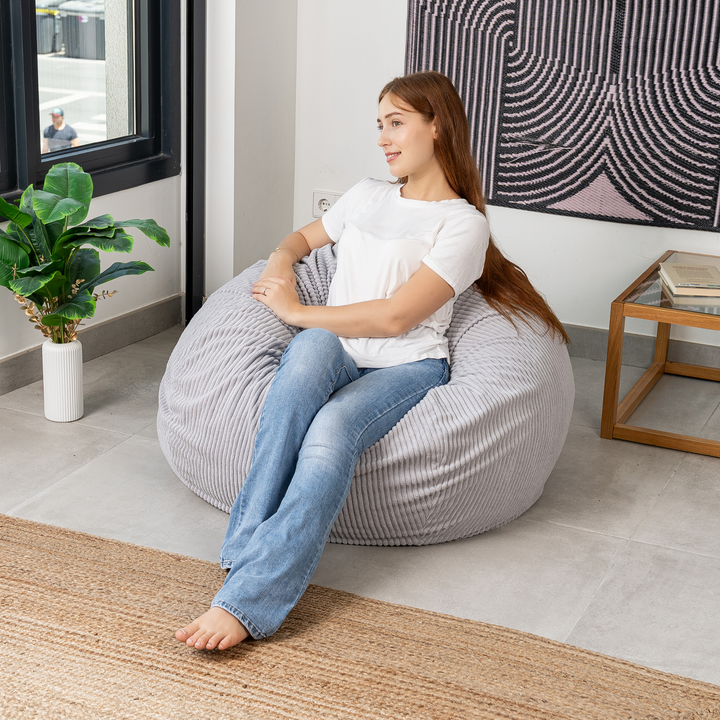 Femme assise sur un pouf poire déhoussable en velours côtelé, dans un salon
