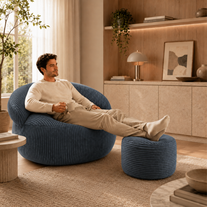 Personne assise confortablement sur un pouf XXL en velours côtelé avec repose-pieds, dans un salon