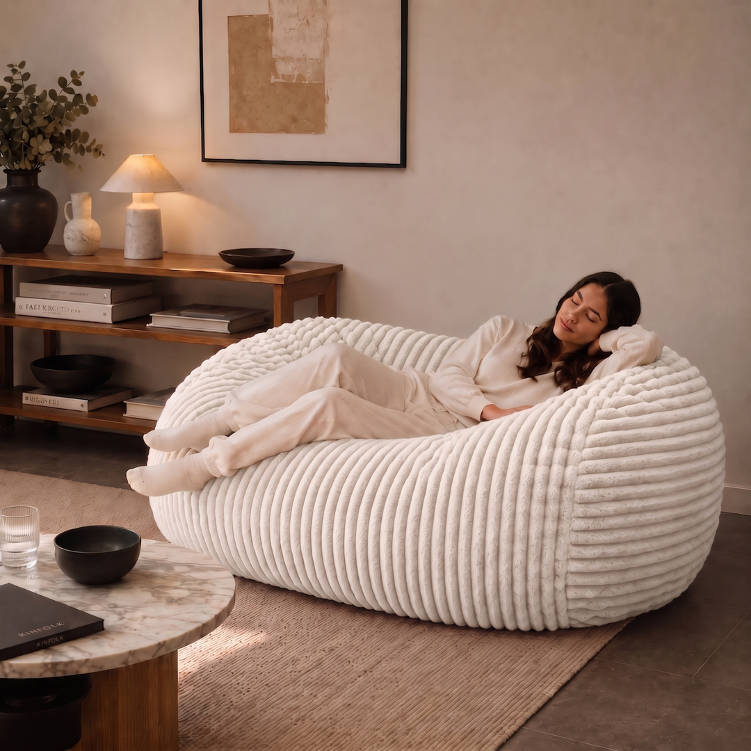 Personne allongée sur un pouf long géant déhoussable blanc cassé en fourrure côtelée dans un salon