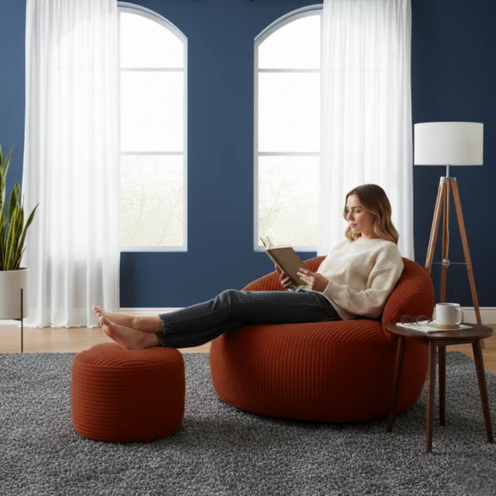 Personne assise confortablement sur un pouf XXL en velours côtelé avec repose-pieds, dans un salon