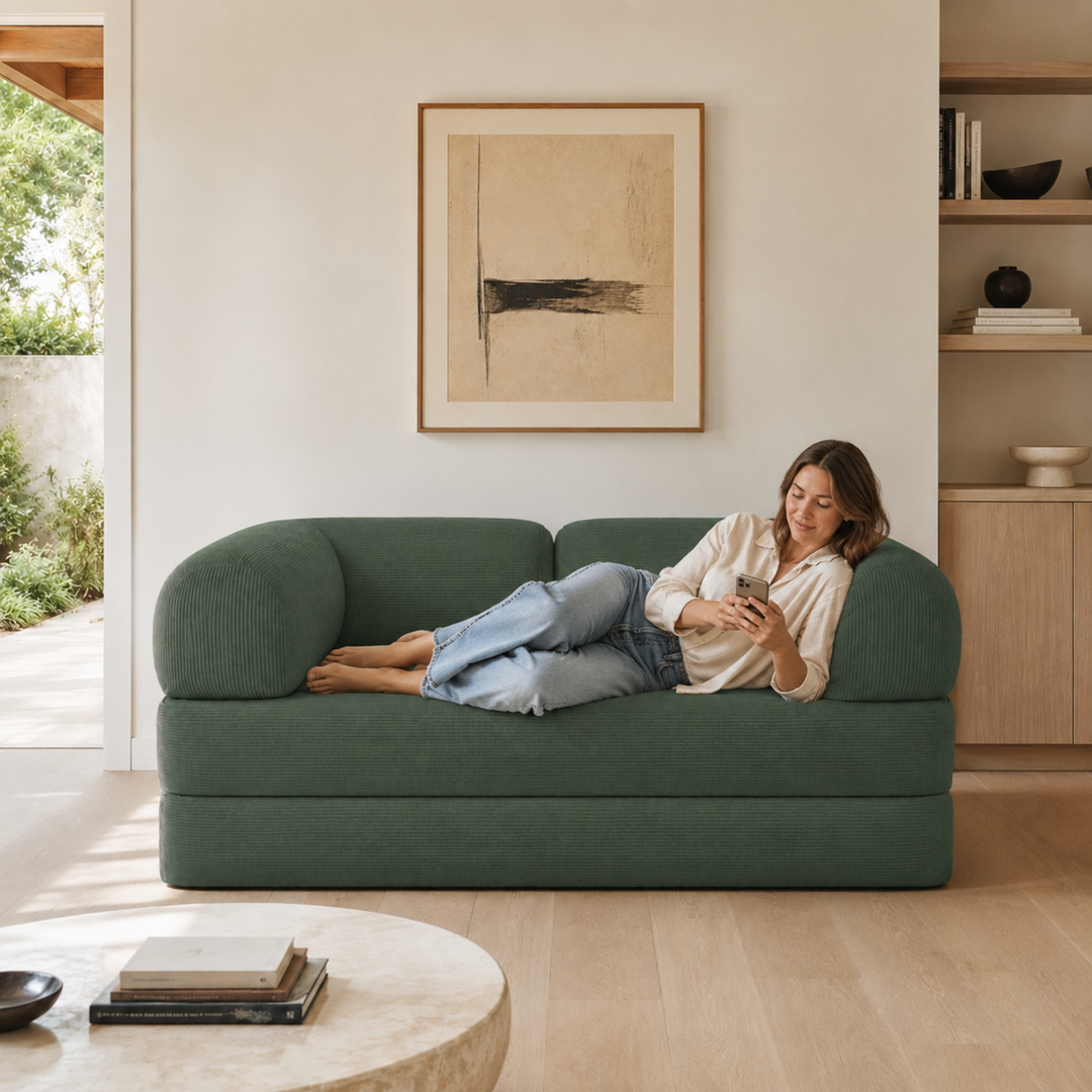 Personne assise sur un canapé-lit 2 places en velours côtelé vert, dossier bas et accoudoirs rembourrés.