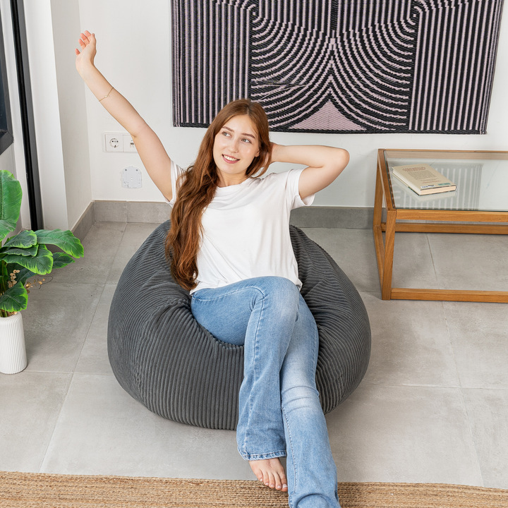 Femme assise sur un pouf poire déhoussable en velours côtelé, dans un salon
