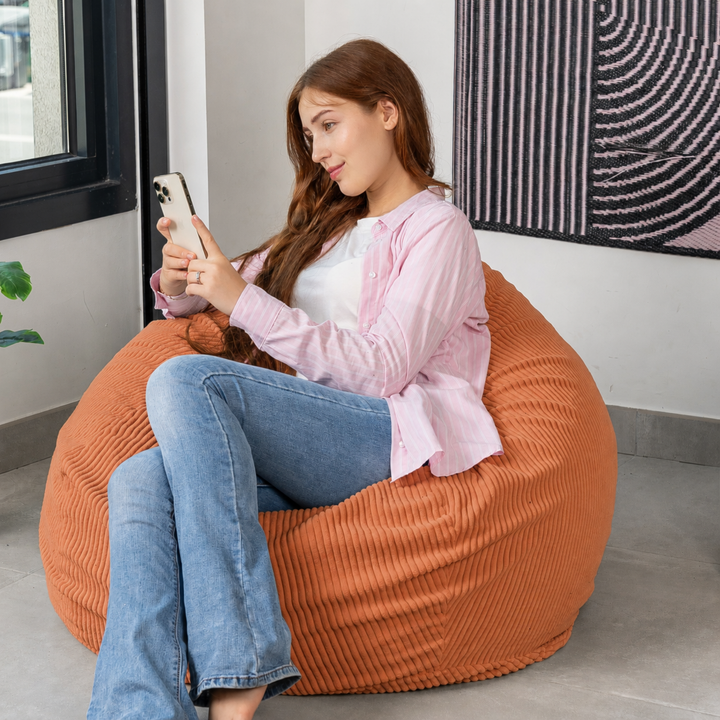 Femme assise sur un pouf poire déhoussable en velours côtelé, dans un salon