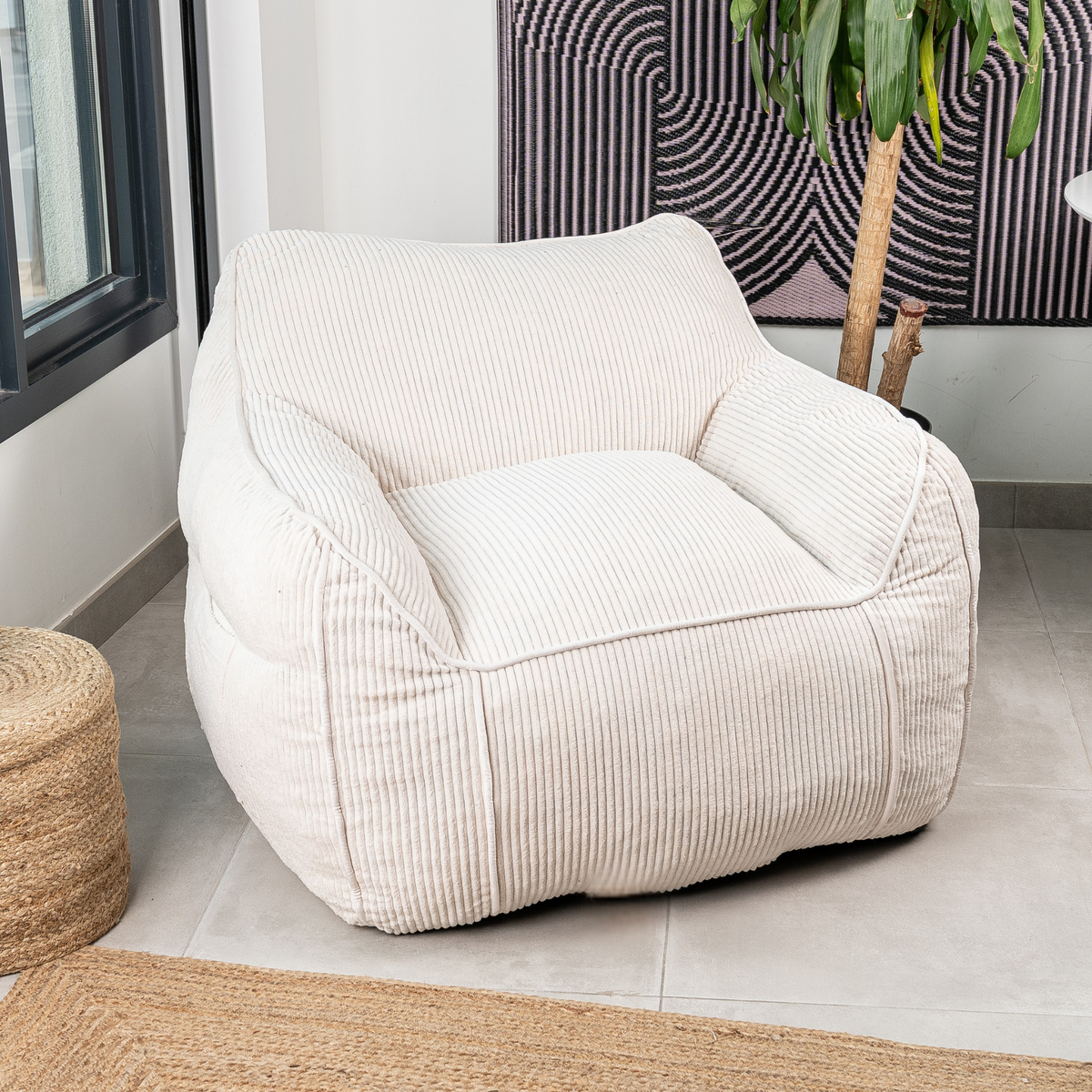 Pouf fauteuil en velours côtelé blanc cassé, dossier et accoudoirs moulés, aspect moelleux, dans un salon