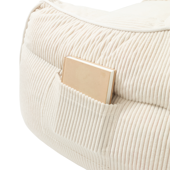 Pouf fauteuil en velours côtelé blanc cassé, détail de la poche de rangement sur le côté.